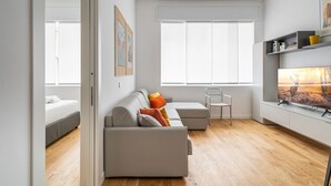 Een moderne woonkamer met een grijze bank, een klein tafeltje en een televisie op een witte dressoir.