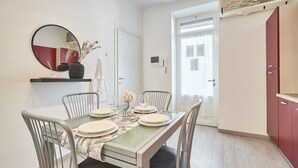 Uma área de jantar com mesa de vidro, cadeiras brancas e espelho na parede.