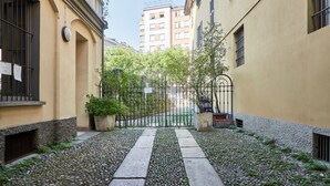 Uma viela estreita com caminho de pedra, ladeada por edifícios com varandas e um portão de metal.
