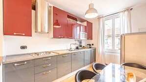Una cocina moderna con armarios grises y rojos, una encimera de madera y una mesa de comedor de vidrio con sillas negras.