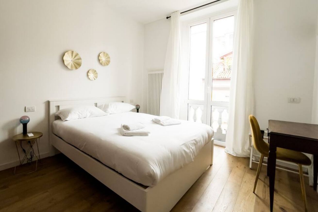 A bedroom with a bed, a bedside table, a chair, and a window with curtains.