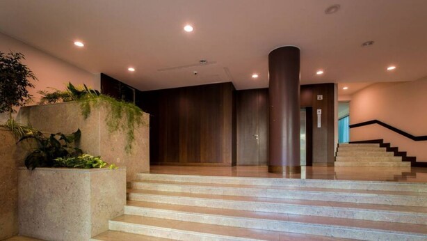 A modern hotel lobby with a marble staircase, a large column, and a plant wall.