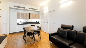 A modern kitchen with white cabinets, a wooden dining table, and a black leather sofa.