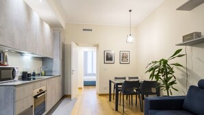Een moderne keuken met een magnetron, fornuis en kasten, die uitkomt op een eethoek met een tafel en stoelen.