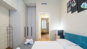 Een moderne hotelkamer met een bed, een garderobe, een handdoekhouder en uitzicht op de gang.