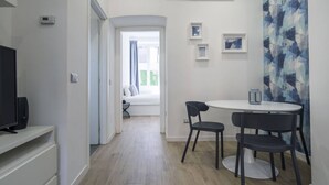 En moderne stue med fjernsyn, spisebord med stole, sofa og et vindue med udsigt til grønne omgivelser.