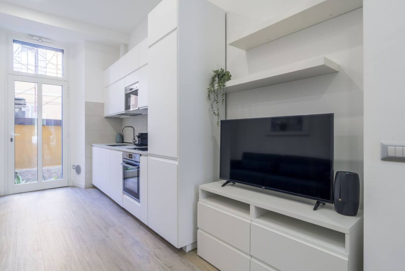 Una cucina moderna con mobili bianchi, forno integrato e un ampio televisore a schermo piatto su un'unità porta TV bianca.