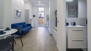Et moderne, lyst værelse med en blå sofa, et spisebord med stole og et hvidt skab med spejl.