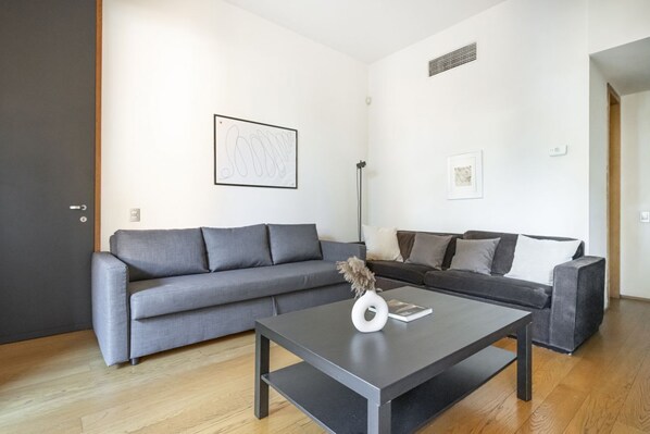 Un salon moderne avec deux canapés gris, une table basse noire et un lampadaire.
