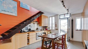 A kitchen with a wooden table and chairs, a staircase, and a window with a view. - Easylife - Attico Duplex Chinatown (Milano)