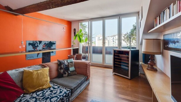 A living room with a sofa, a coffee table, and a bookshelf. There is a large window providing a view of the outside. - Easylife - Attico Duplex Chinatown (Milano)