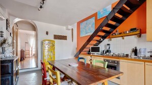 A compact kitchen with a wooden table and chairs, a yellow refrigerator, and a staircase with orange accents. - Easylife - Attico Duplex Chinatown (Milano)