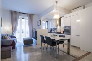 A modern kitchen with white cabinets, a dining table with chairs, and a pendant light.