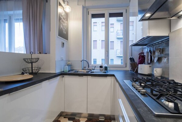 A modern kitchen with white cabinets, a black countertop, a gas stove, and a window with a view of buildings.