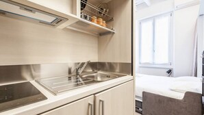 A compact kitchenette with a stainless steel sink, a built-in stovetop, and a shelf above the sink. - Easylife - Cozy studio apartment in Porta Venezia (Milano)