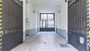 A corridor with a tiled floor leading to a large door with metal gates. - Easylife - Cozy studio apartment in Porta Venezia (Milano)