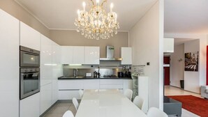 A modern kitchen with white cabinetry, a large island, stainless steel appliances, and a chandelier.