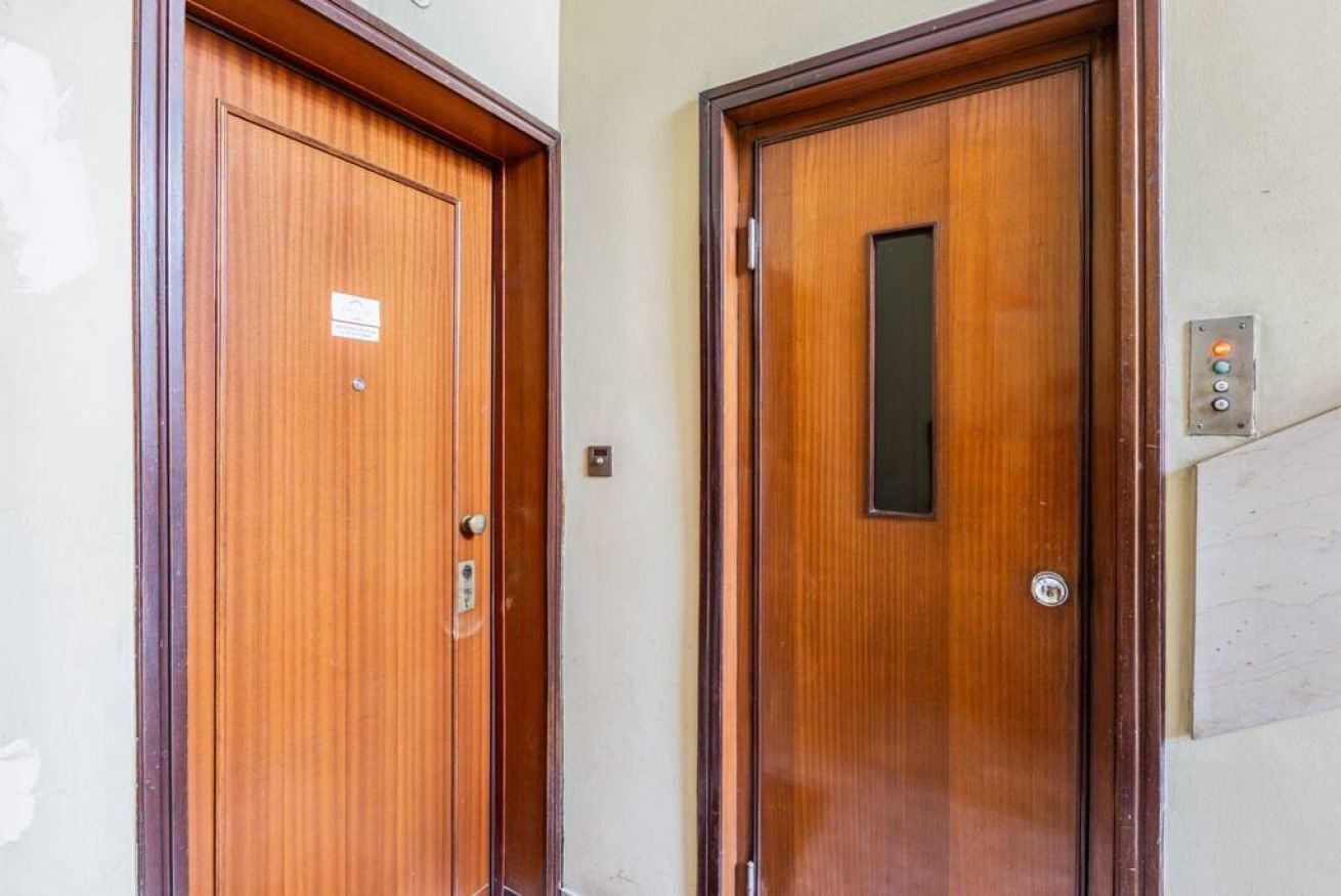 Deux portes en bois, chacune dotée d’une fenêtre verticale, un interrupteur fixé au mur et une petite pancarte sur la porte de gauche.