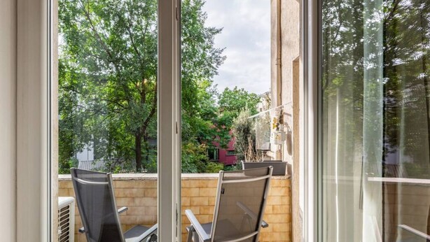 A balcony with two chairs, a view of trees and a building in the background.