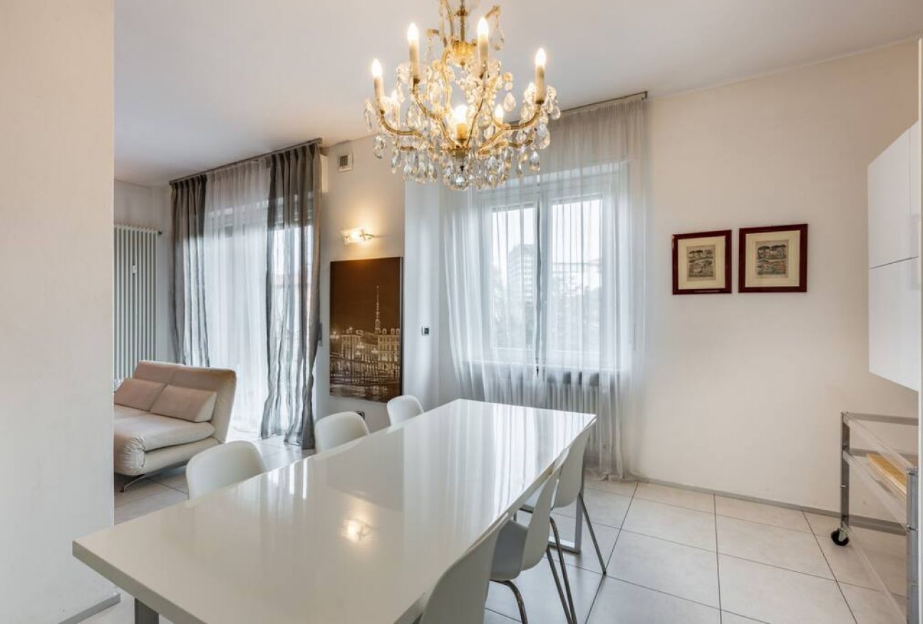 Un comedor moderno con una mesa larga, sillas blancas, una araña y un sofá.