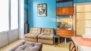 Een kamer met een blauwe wand, een beige bank, een houten bureau en een kleine tafel.