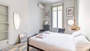 Een slaapkamer met een bed, een radiator, een lijst met een afbeelding, een spiegel en een deur.