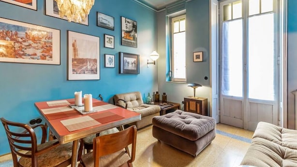 Een eetgedeelte met een tafel gedekt voor twee personen, een bank en een groot raam met gordijnen.