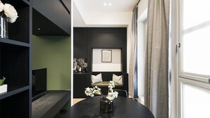 A modern living room with a black round table, a black sofa, and a green accent wall. - Easylife - Elegant studio apartment in Corso Magenta (Milano)