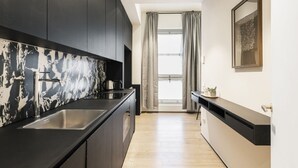 A modern kitchen with dark cabinets, a marble backsplash, and a stainless steel sink. - Easylife - Elegant studio apartment in Corso Magenta (Milano)