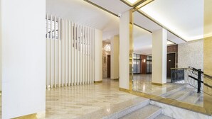 A modern hotel lobby with marble flooring, a glass staircase, and a decorative wall with vertical panels. - Easylife - Elegant studio apartment in Corso Magenta (Milano)