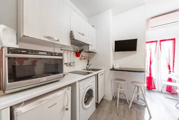 A compact kitchen with a microwave, washing machine, and a small bar area with stools.