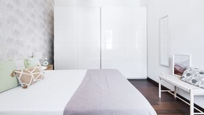 Un dormitorio con cama, armario, banco y pared con diseño geométrico.