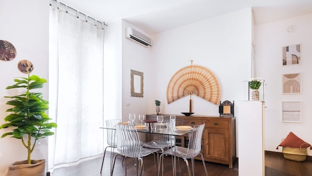 Un comedor con una mesa de vidrio y sillas, un mueble de madera y un abanico decorativo.