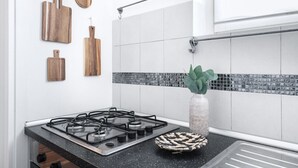 Una cocina con estufa a gas, baldosas blancas, encimera negra y tablas de cortar de madera en la pared.