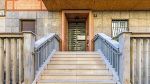 Un conjunto de escalones de piedra que conducen a una puerta de madera con una verja metálica, flanqueados por barandales de piedra.