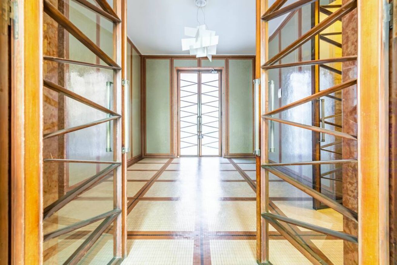 Un couloir doté d’un sol carrelé et de portes vitrées à cadre en bois qui donnent sur une pièce.