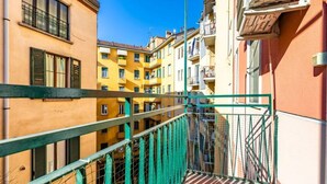 Un balcón estrecho con barandilla metálica verde, con vistas a una hilera de edificios amarillos y anaranjados con balcones.