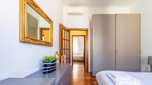 Una habitación de hotel con una cama, un espejo grande, una mesita de noche con una planta y un armario.