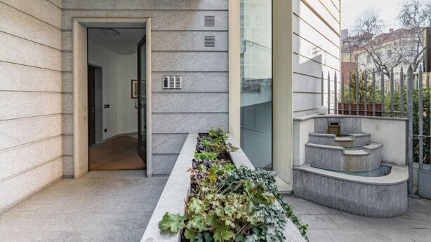 Une entrée moderne, avec un bac à plantes en béton agrémenté de verdure, une porte en verre et un escalier en métal.