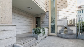 Une entrée moderne avec une façade en pierre, un petit espace extérieur aménagé avec des plantes et un escalier menant à l’entrée.