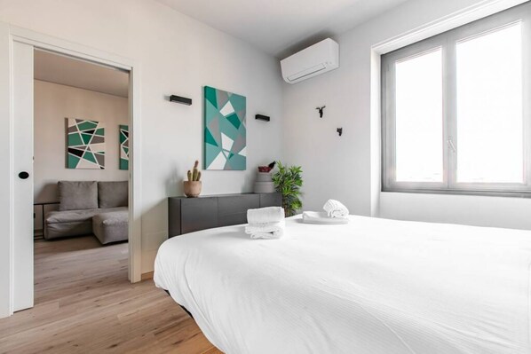 Un dormitorio moderno con una cama grande, un pequeño rincón de estar y un ventanal con luz natural.