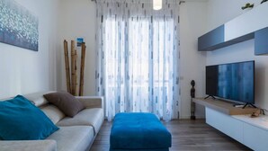 Una sala moderna con un sofá, un reposapiés y un televisor de pantalla plana.