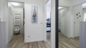 Un pasillo con piso de madera, un cuadro de un velero en la pared, una puerta blanca y una pared blanca con un interruptor de luz.