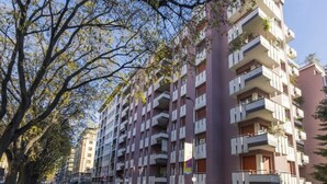 Un edificio residencial de varios pisos con balcones, coches aparcados y árboles a lo largo de la calle.