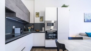 Una cocina moderna con armarios blancos, un microondas integrado y un horno. Hay una mesa de comedor con sillas y una pequeña zona de estar con un sofá.