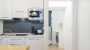 Une cuisine moderne avec des meubles blancs, un four à micro-ondes, une bouilloire et un lave-linge.