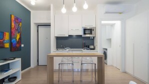 Une cuisine moderne avec des meubles blancs, un four à micro-ondes et un lave-linge à l’arrière-plan. On peut voir trois tabourets de bar devant le comptoir de la cuisine.