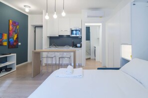 A modern hotel room with a bed, a small kitchenette, and a dining area.