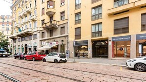 Straßenansicht mit einem gelben Gebäude, Geschäften und parkenden Autos.