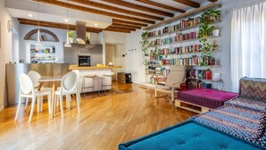 A modern living space with exposed wooden beams, a kitchen area, a dining table with chairs, a bookshelf filled with books, and a cozy seating area with a patterned rug. - Easylife - Splendid penthouse in Porta Venezia (Milano)
